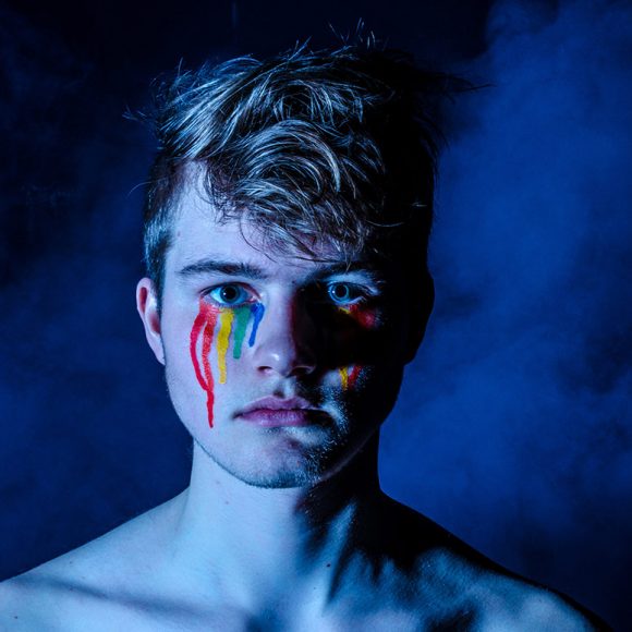Portrait of a young artist with colorful paint on his face.