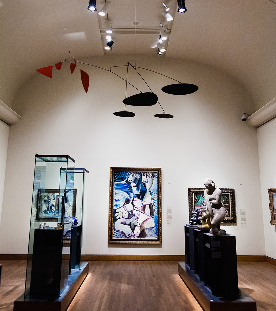 Sala museale con dipinti, scultura e teche espositive.